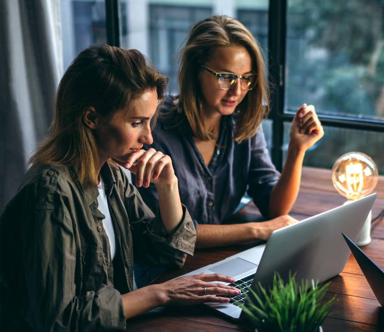 two young professional women confer at a table and use a laptop