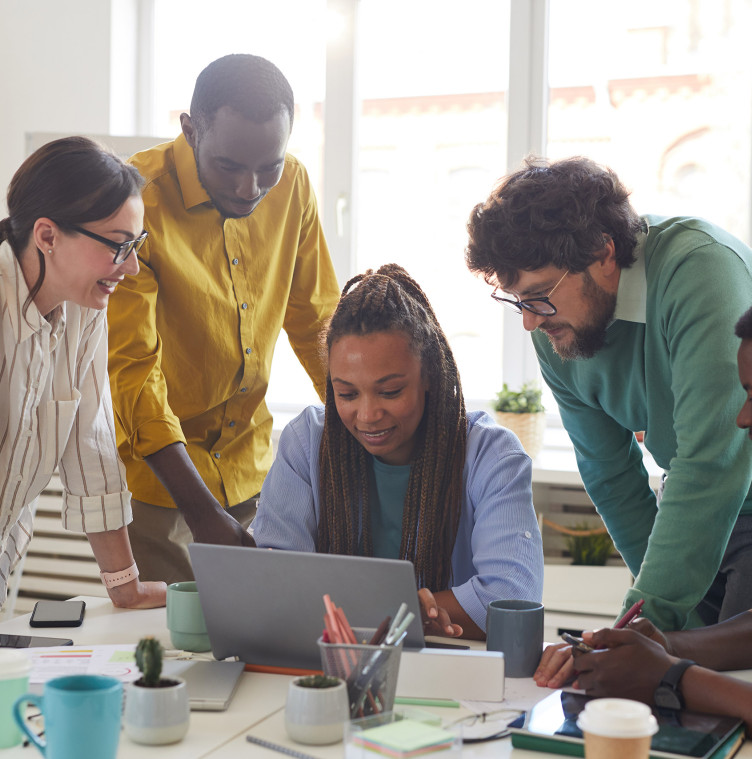 four colleagues surround a young black woman looking at her laptop screen